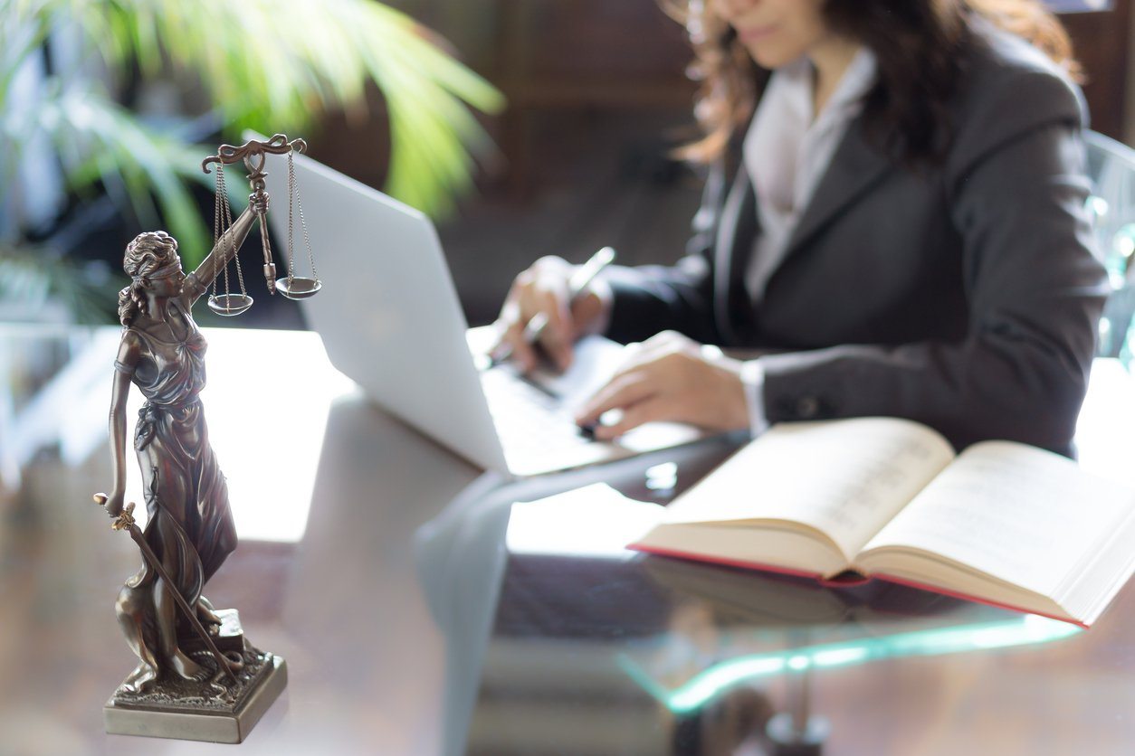 A professional woman in a business suit working at a desk with a laptop computer.