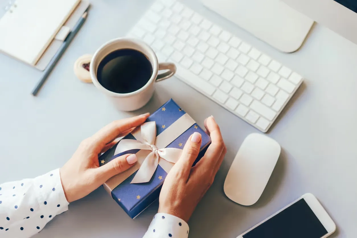 Two hands hold a wrapped gift at a desk in an immigration law firm office, symbolizing the use of physical marketing strategies to enhance brand visibility.