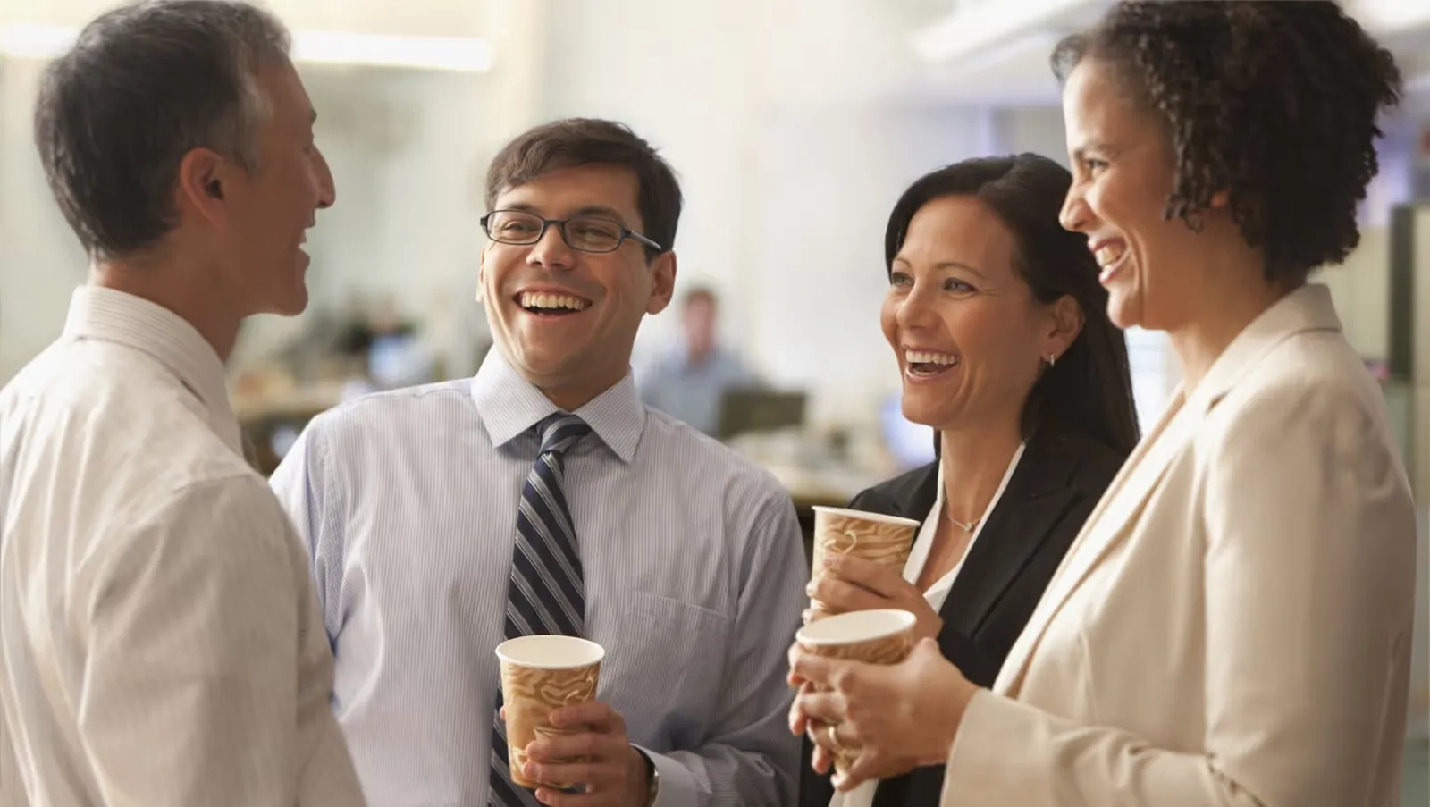 Four professionals smiling and holding coffee cups, exuding confidence and camaraderie.