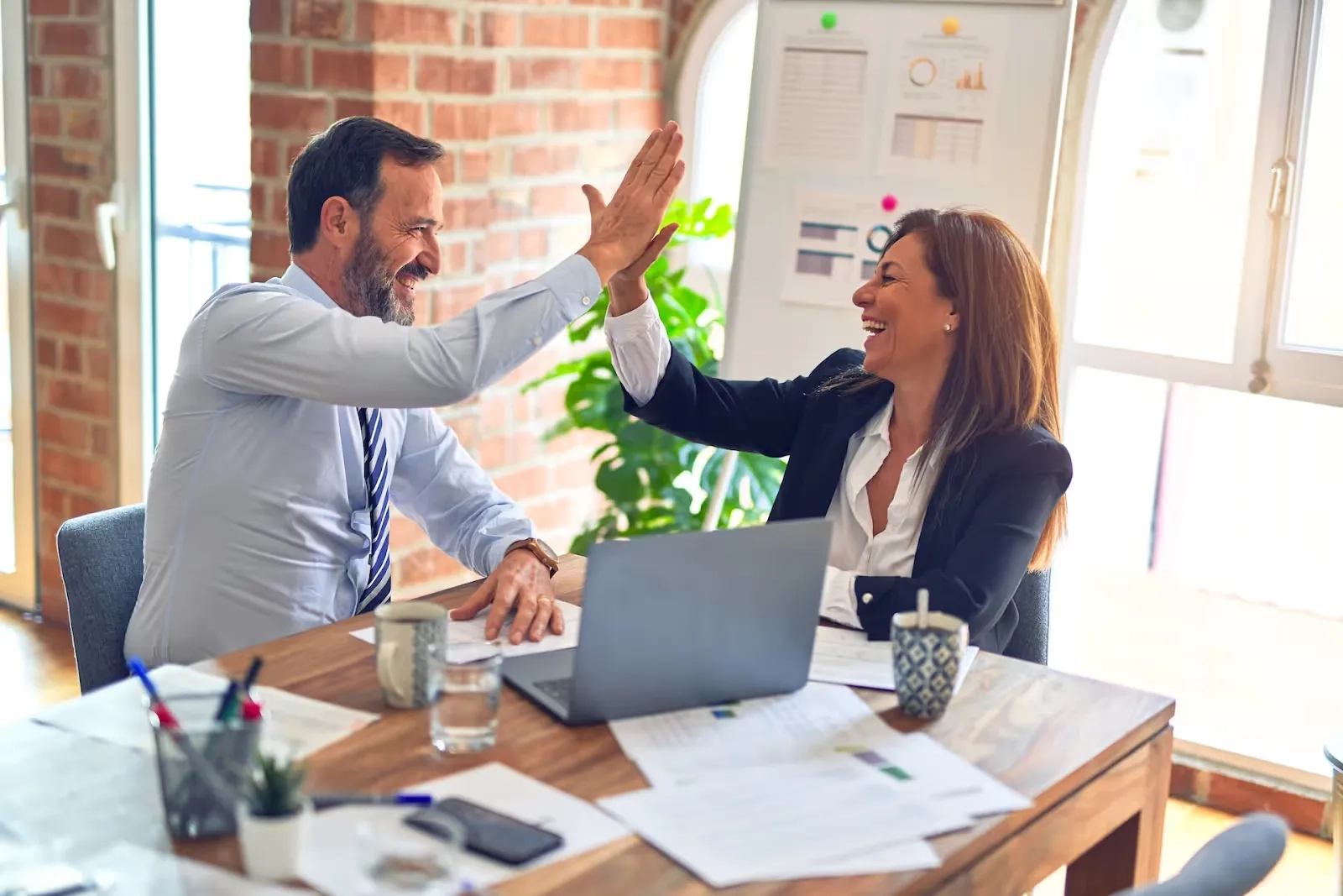 Two business professionals celebrating success with a high five at a desk.