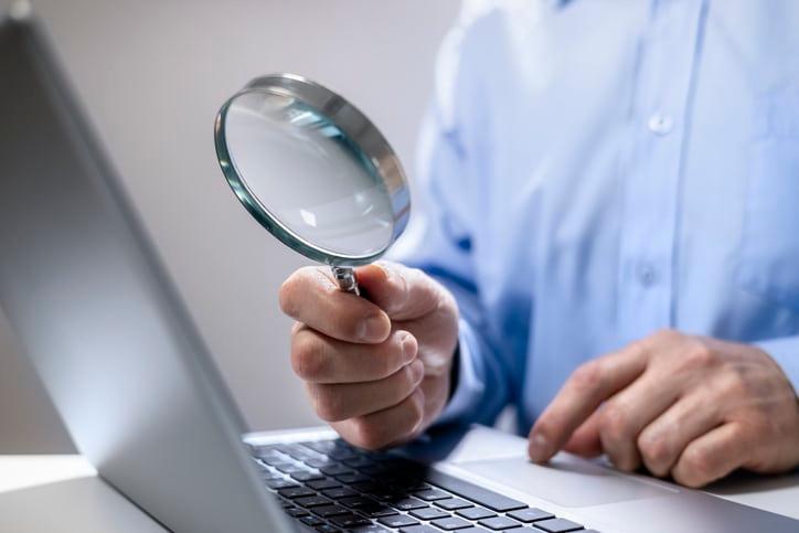 Person holding magnifying glass over laptop