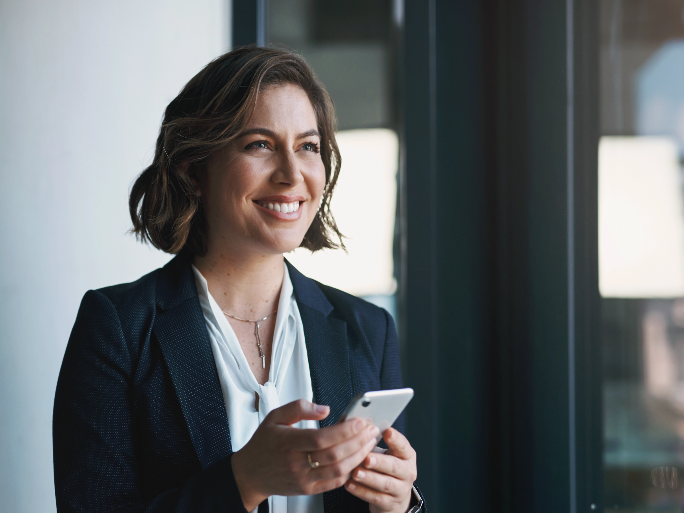 A woman smiles while looking up from her cell phone