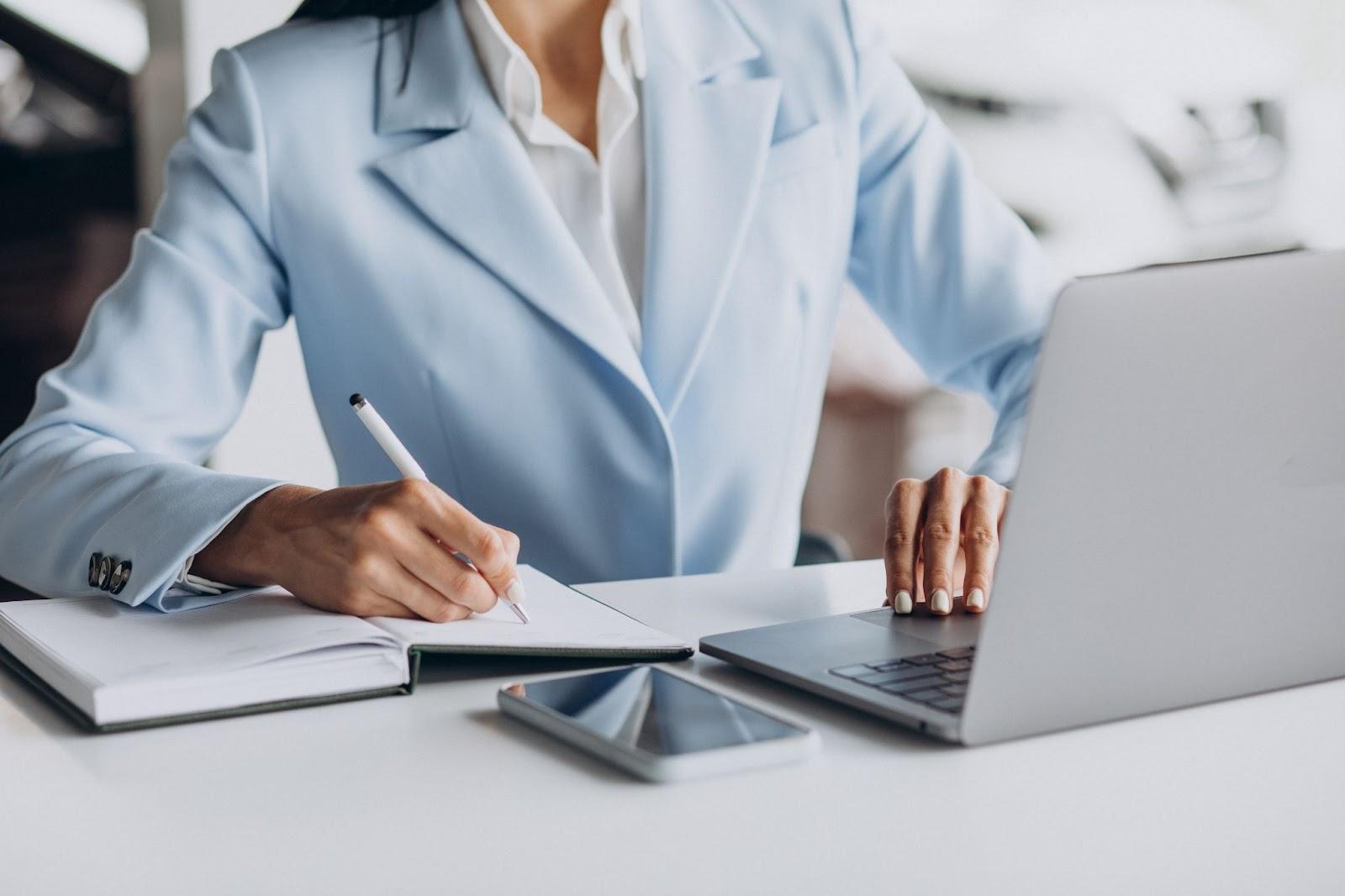 woman in front of a lap top writing in notepad