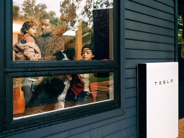 man and his children in the window with a Tesla home battery outside