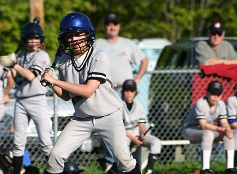 Child in baseball uniform carries bat to plate
