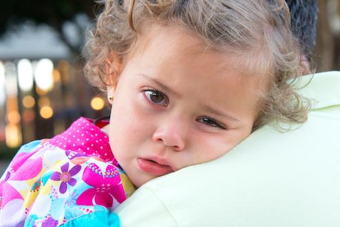 Upset toddler leans on parents shoulder