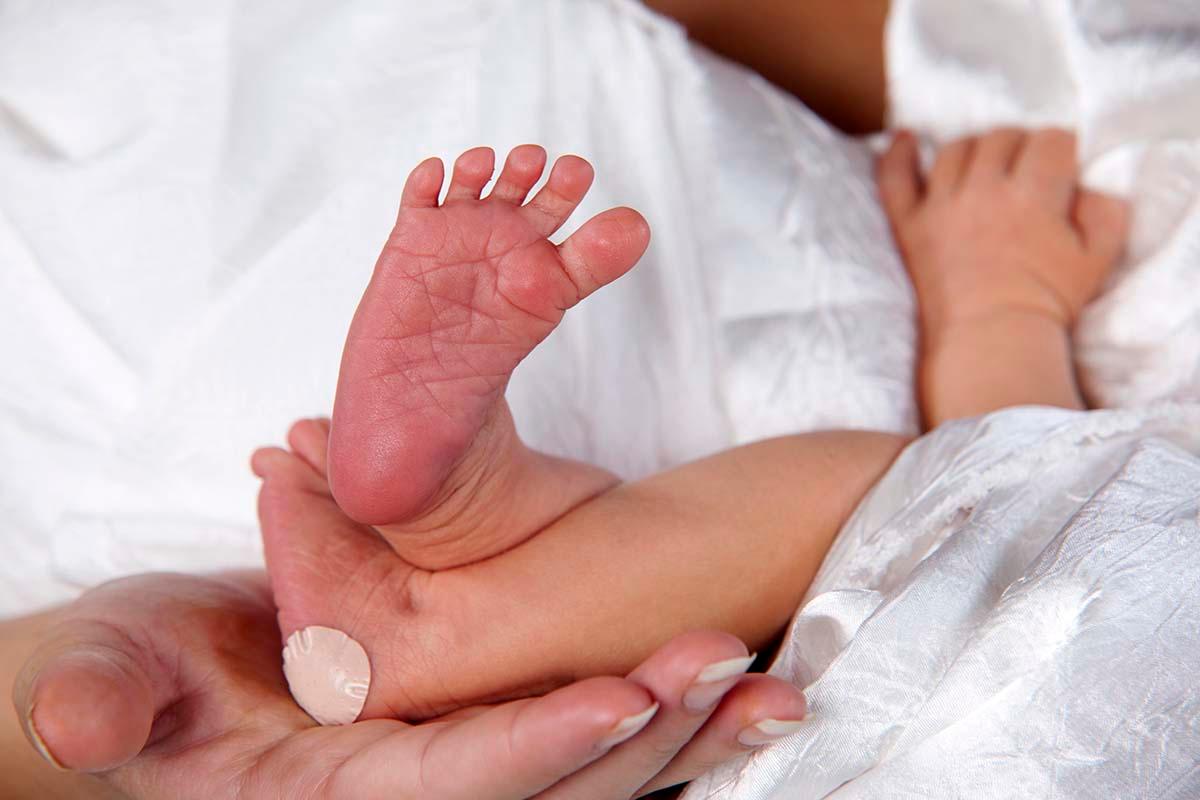 Loving mom holds newborn feet, with bandaid from heel stick