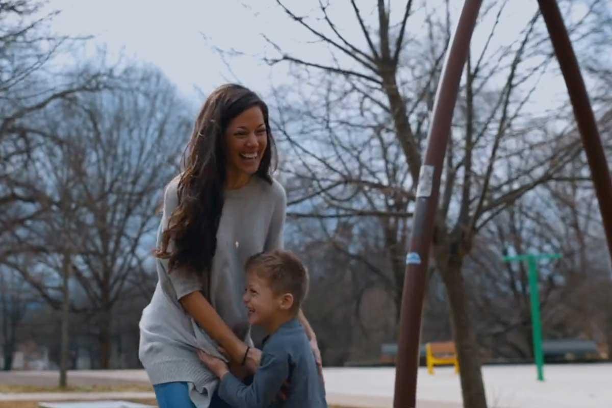 Now healthy mom hugs her young son in front of a swingset on a sunny day