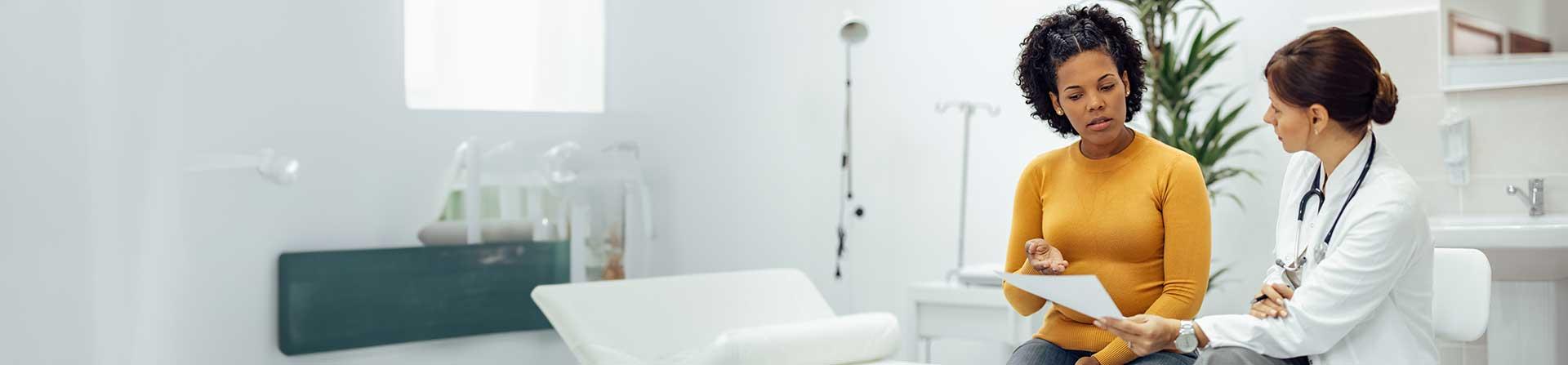 A woman sitting in a clinic room talking with a doctor