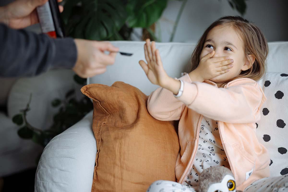 Close up of a small girl refusing to take cough syrup from a syringe. 