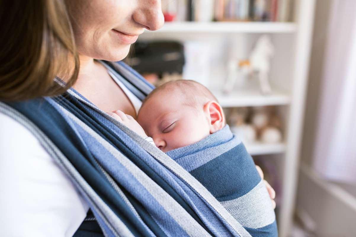 Mom smiles at newborn, being carried on her chest in a wrap