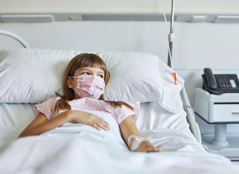 young girl in hospital bed wearing mask