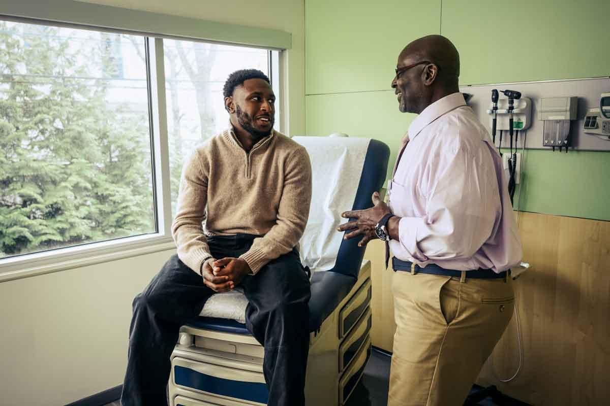A young man sitting in a medical office talking about a medical device recall with a doctor who is standing