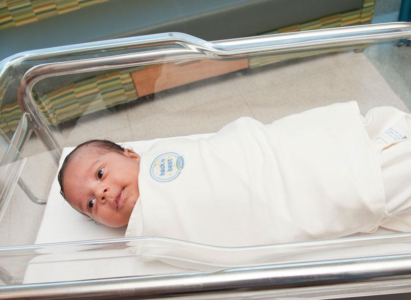 An infant wrapped in a safe sleep swaddle lays in a hospital bassinet