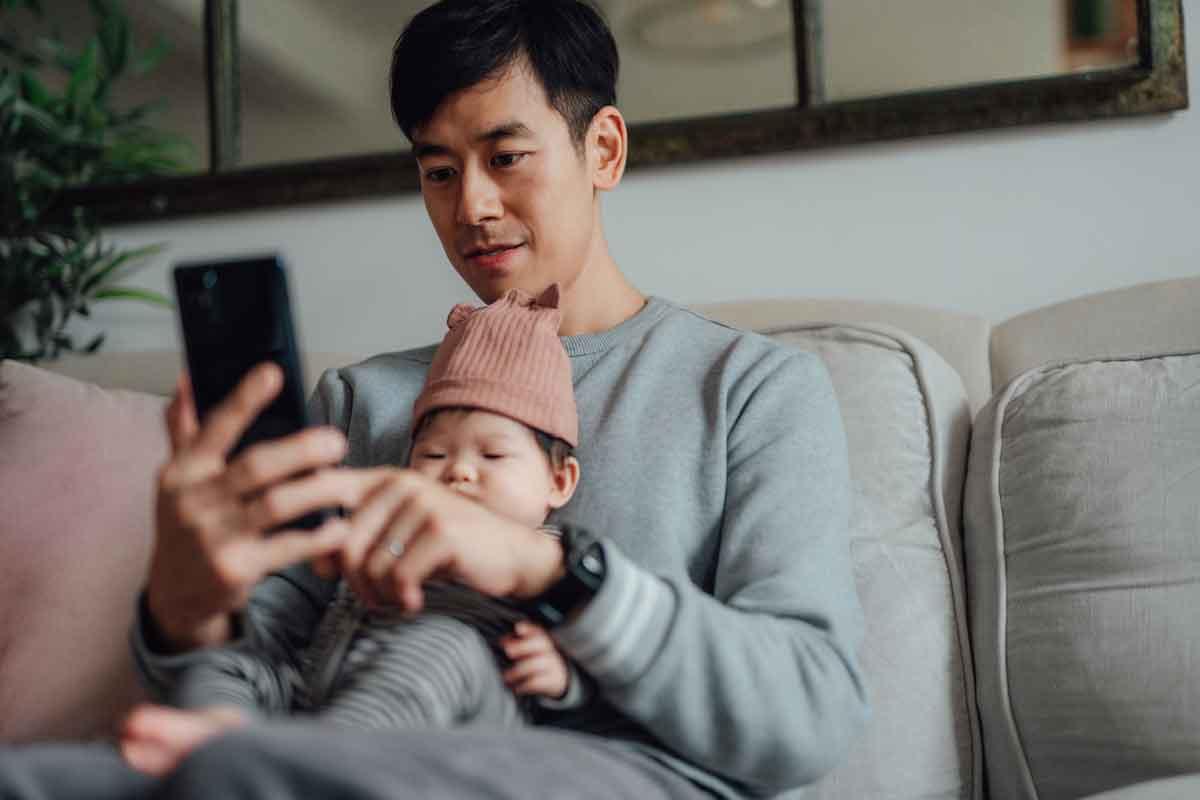 A man sitting while holding a baby and looking at his phone
