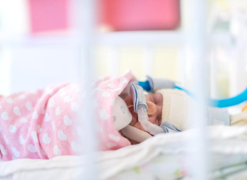Premature baby on breathing support in NICU wrapped in pink swaddle