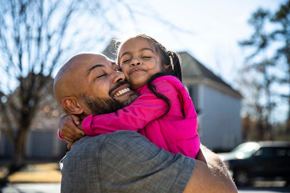 Father holds child up for hug while standing outside