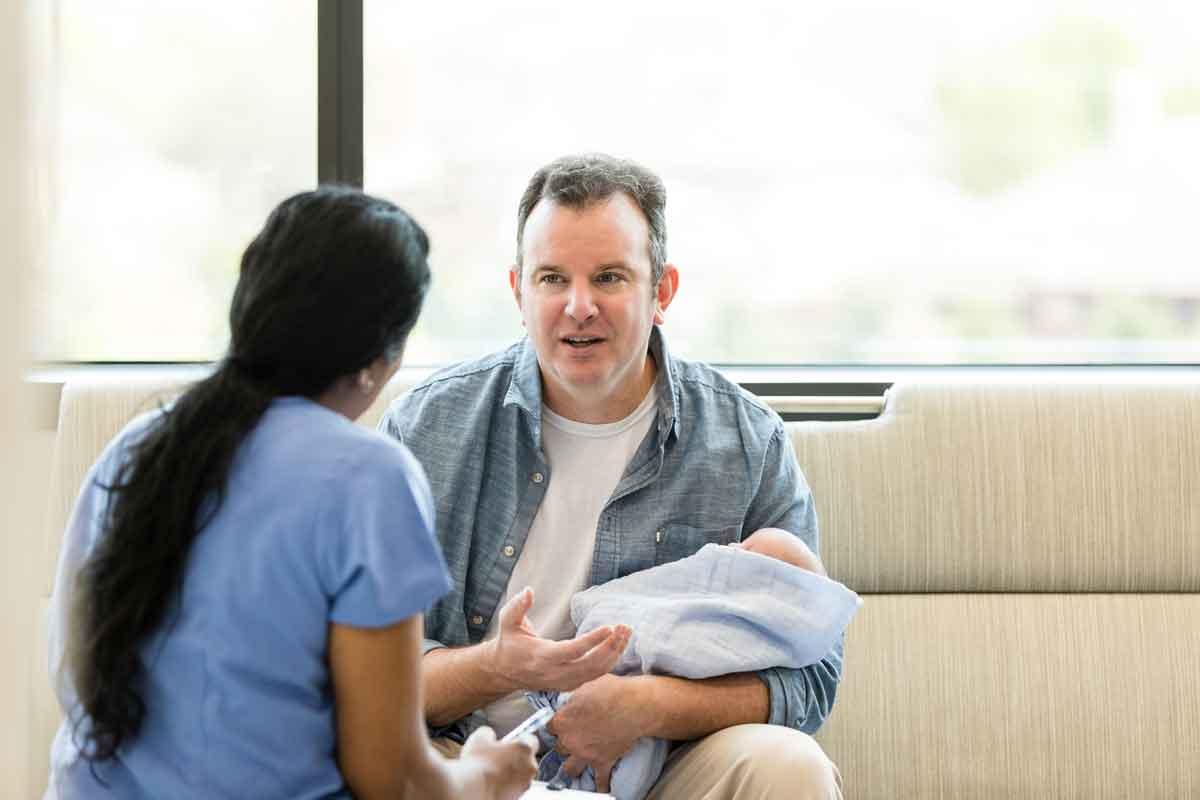 A father sitting on a couch talking to a healthcare provider about circumcision