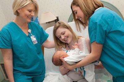 Mom looks lovingly at newborn while two nurses help