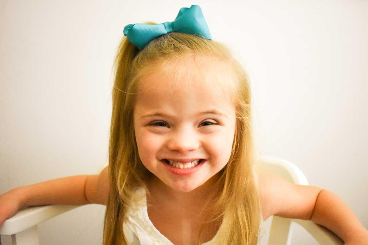 Young blonde child with blue bow on her head smiles for the camera