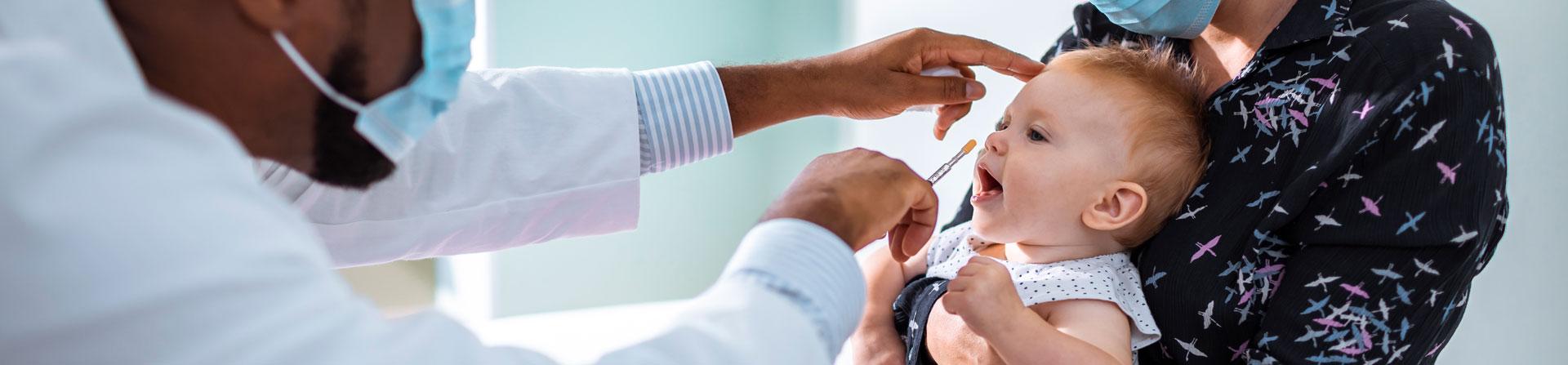 A baby being examined by a doctor using an instrument in is hand. A woman is holding the baby.