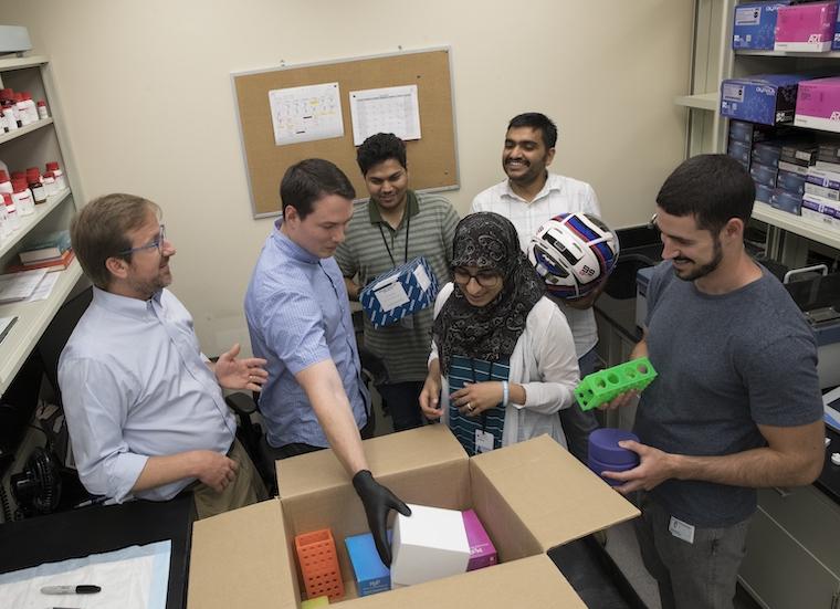 Greg Medlock's work aims to determine how to grow microbes most efficiently. It's similar to figuring out how to most effectively fit many items into a box. (Greg is wearing black gloves in the picture above; he is joined by other members of the lab overseen by Sean Moore, MD, at left.)
