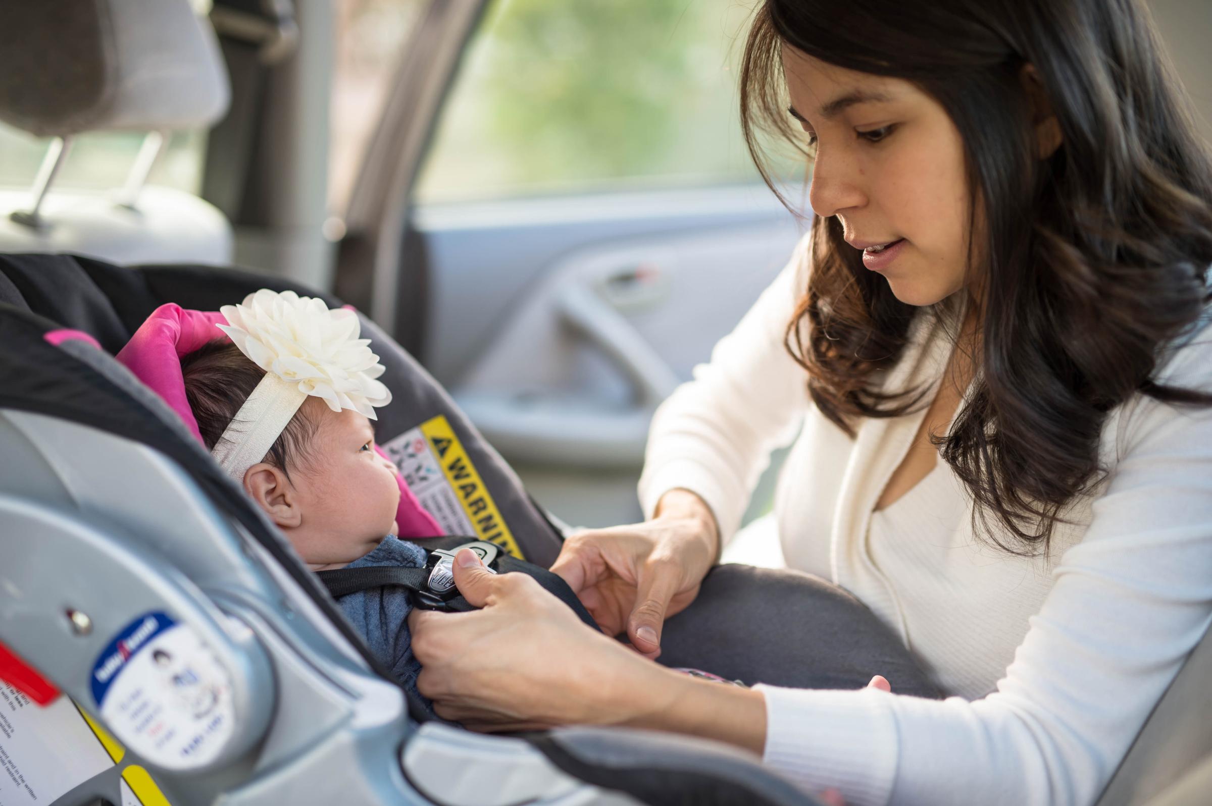 Mom buckling in her newborn baby to a car seat