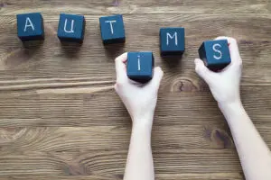 Hands arrange letter blocks to spell autism