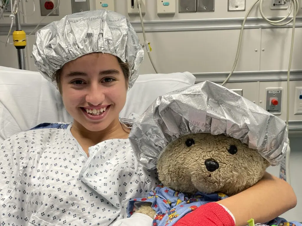 Olivia and teddy bear wear matching surgical caps as they prep for surgery
