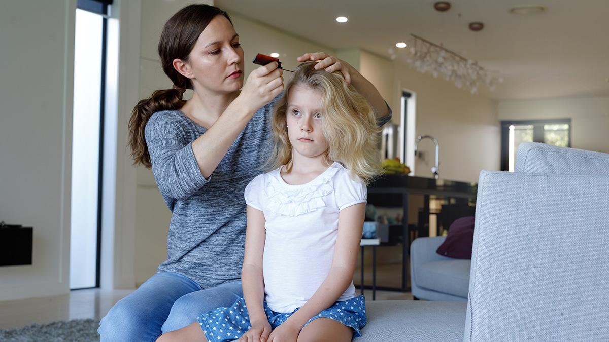 A woman and child sitting on a couch while the woman combs the child's hair