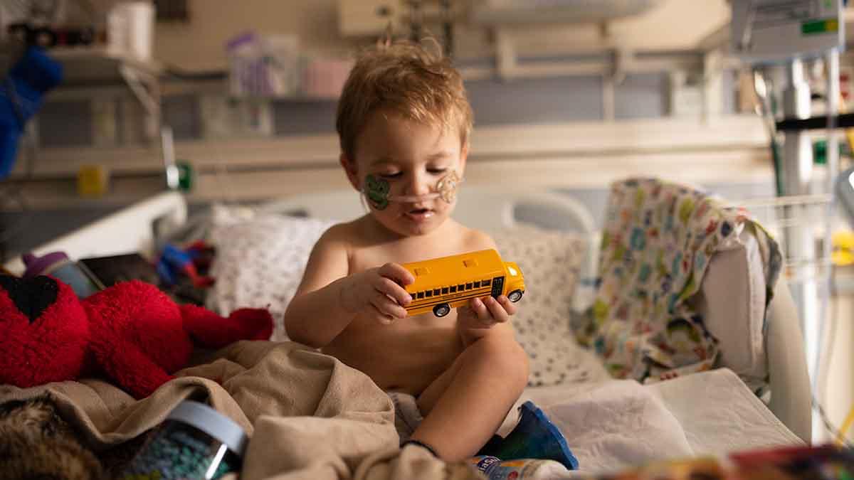 Toddler with oxygen nasal cannula plays with a toy school bus