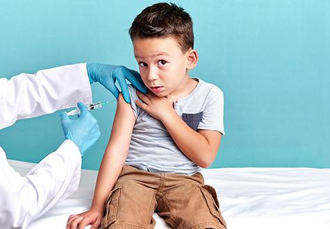 Young boy with sleeve rolled up looks at camera as provider gives a shot