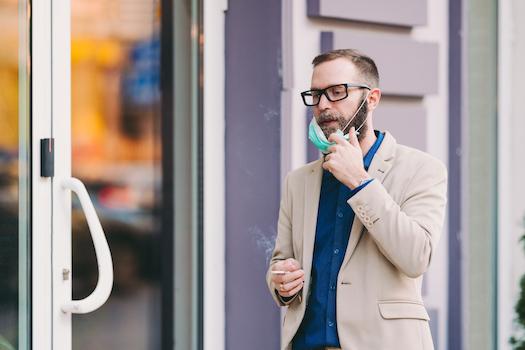 man removing his face mask to smoke a cigarette during coronavirus pandemic