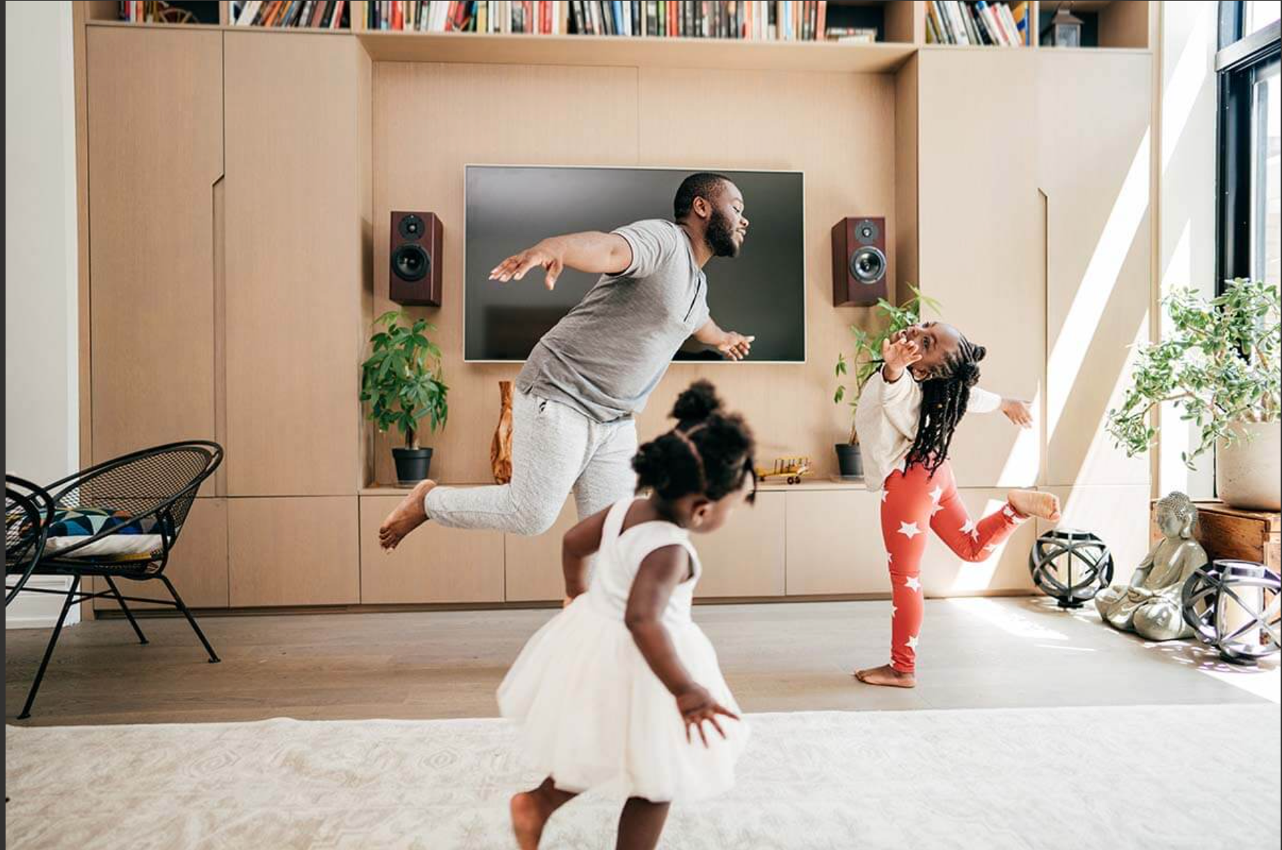A father dances in the living room with his two young daughters