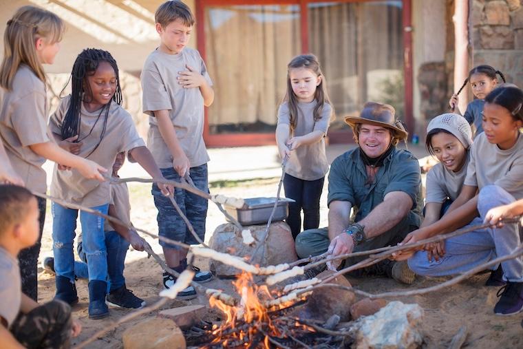 Group of kids and camp counselor roast marshmallows over a fire