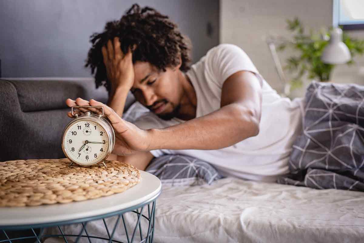 A man waking up, reaching out to stop an alarm clock