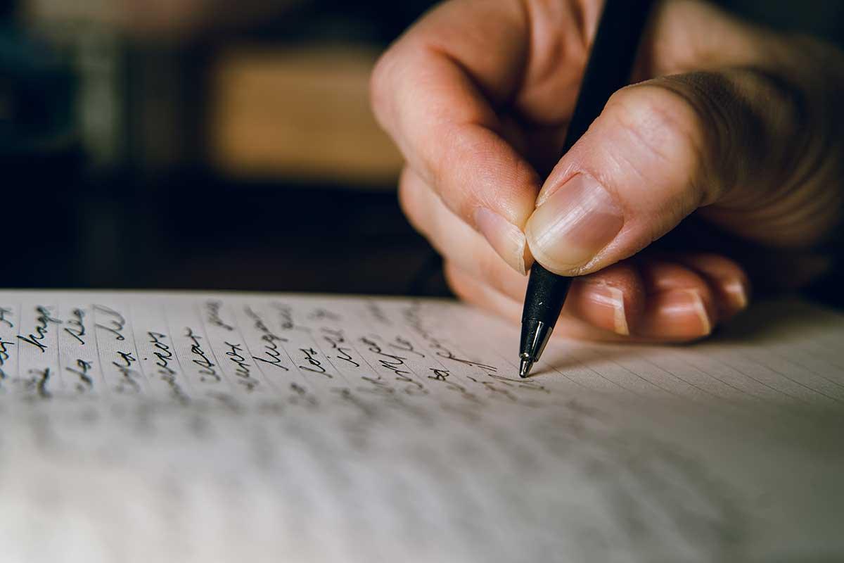 A hand holding a pen and writing on paper