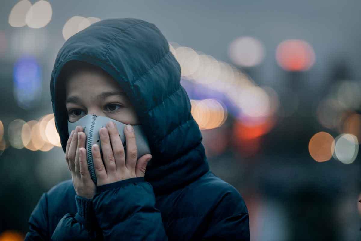 A young person holding a mask on their face to protect against bad air quality