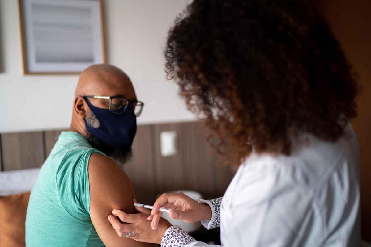 A man receiving a COVID vaccine in his left arm. A nurse is injecting him with a needle.