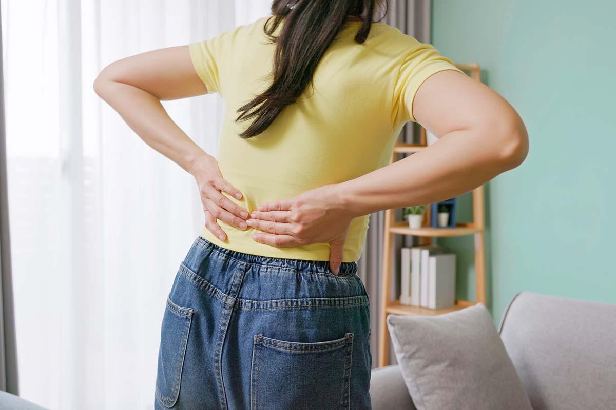 close up woman feels lower back pain in living room at home