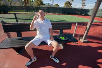 Senior male tennis player drinking water while relaxing on court