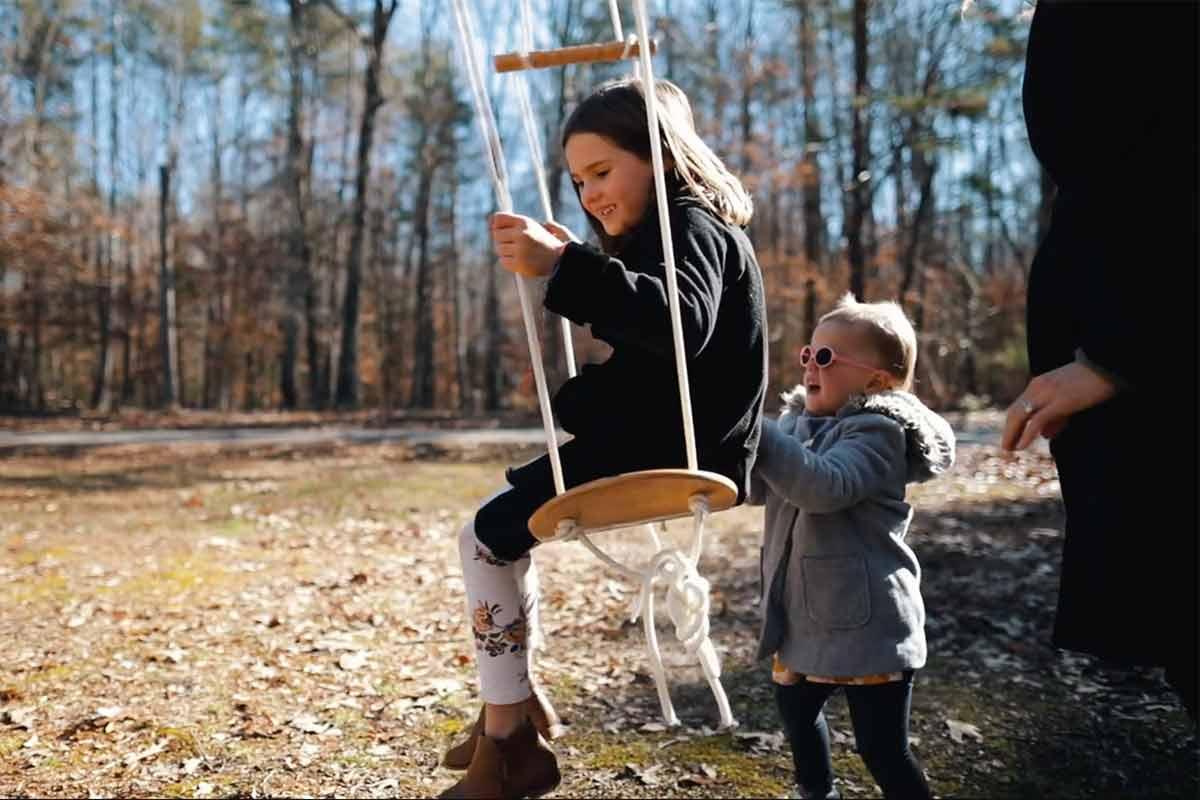Younger sister pushes her big sister on a swing