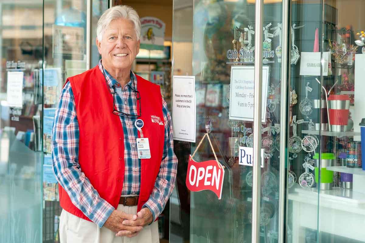 Dave Kohstall in red volunteer vest poses outside of the UVA Health gift shop 