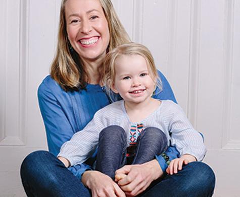 Samantha Dabney sitting and smiling while holding her daughter in her lap, who is also smiling.