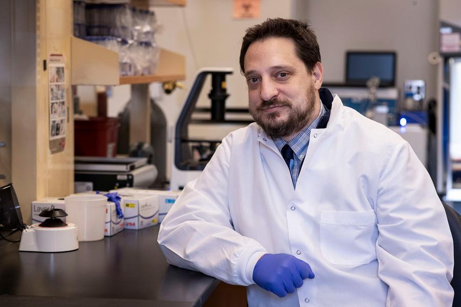 Bradley Gelfand, in his lab wearing white coat smiles at camera