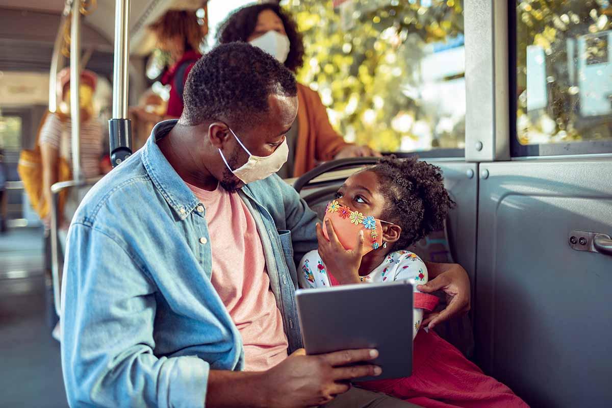 adult and child wearing masks on bus, looking at tablet