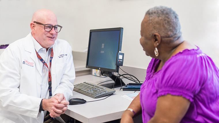 Doctor sitting at computer talks to patient