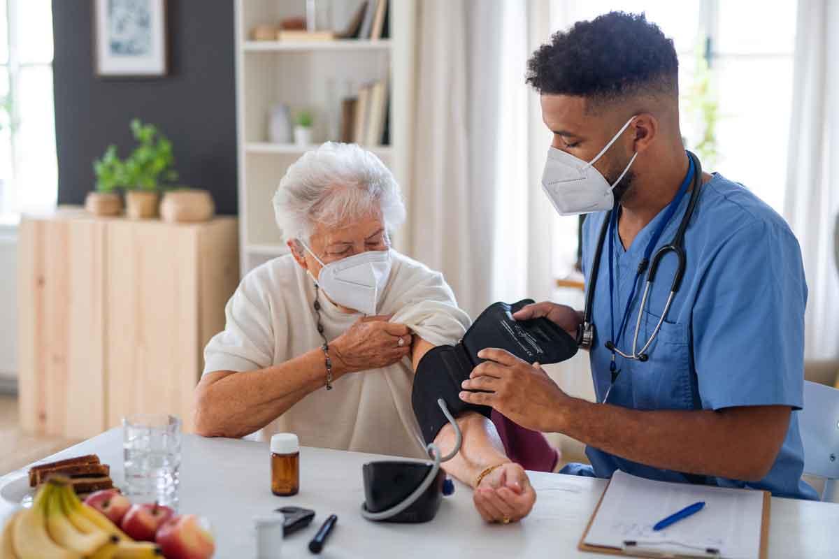 An older woman getting checked for heart disease by having a blood pressure cuff put on her arm by a young Black doctor