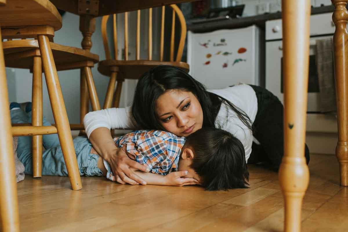 A mother comforting a child having PTSD symptoms, who is laying face down.