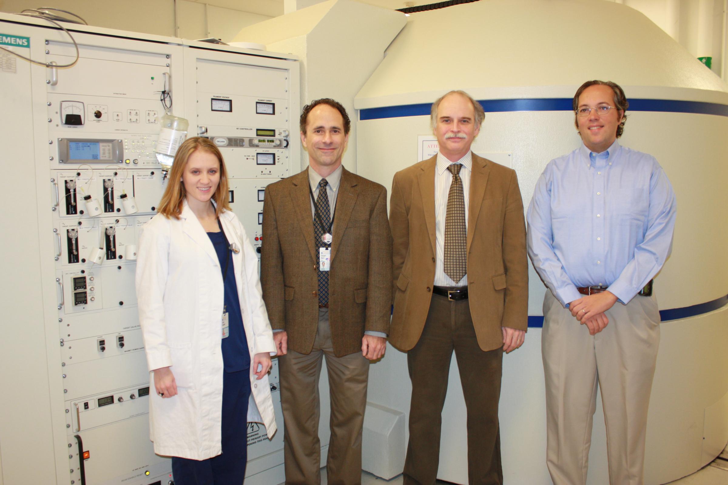(l to r) Dr. Darci Sidwell, Dr. Stuart Berr, Dr. Brent French and Dr. James Stone in front of the cyclotron, a circular particle accelerator that weighs over 50,000 pounds. (Click on photo for high resolution)